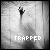 Pixelated grayscale image of a hand reaching upward from a shadowy lower area toward a bright background, with the word "TRAPPED" in blocky text at the bottom.