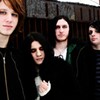 Four people stand closely together in a group pose, with one person holding a white object in their hands.