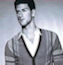 Static grayscale icon of a person in a V-neck sweater with visible facial features and hair, cropped to show upper torso against light background.