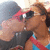 Two figures in close physical proximity, one wearing dark sunglasses and a red headband, the other with brown hair tied back, both partially visible against a light background.