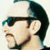 Pixelated static icon of a person's profile with dark hair, glasses, and beard against light background.