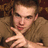 Pixelated image of a person with light skin and brown hair wearing a brown jacket, making a hand gesture with fingers extended toward the viewer.