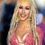 A pixelated image of a person with long blonde hair wearing a pink dress, smiling with mouth open, against a blurred background with dark and light areas.