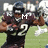 A football player in a dark uniform with number 2, helmet, and shoulder pads holding a ball on a grass field.