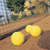 Static 50x50 pixel icon showing two yellow tennis balls on a brown court with blurred green trees and blue sky in the background, rendered with low-resolution pixelation.