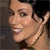 Pixelated close-up of a person's face showing a smiling expression, dark hair, and a light-colored necklace against a dark background.