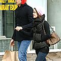 Static image of two people walking outdoors with shopping bags, partially obscured by yellow text overlay in the top-left corner.