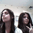 Two women with long dark hair in a room with ceiling lights and framed pictures, one making a peace sign.