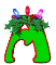 Green letter M with red outline, holly wreath on top, three colored lights (blue, red, purple), and a white triangular cutout in the center.