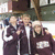 Three figures in dark uniforms with white accents stand side-by-side against a blurred background, each wearing light-colored headgear.