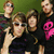 Four pixelated figures in dark clothing pose together against a green background, one holding a pink object.