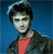 Pixelated portrait of a person with dark hair against a blue background, wearing a dark jacket over a red shirt.