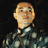 Pixelated static image of a person with light brown hair wearing a dark green patterned shirt and white collar against black background.