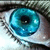 Pixelated close-up of a human eye with blue-green iris, black pupil, and visible eyelashes against light skin tones.