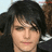 Pixelated image of a person with dark hair and light skin, wearing a dark shirt with white accents, with text at the bottom.