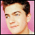 Pixelated close-up of a person's face with light skin, brown hair, and a pink background, cropped to show shoulders and head.