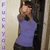 A person in a purple top and dark pants stands against a light wall, making hand gestures near their face with vertical text on the left.