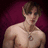 Pixelated image of a shirtless person with short brown hair wearing a silver necklace, set against a dark purple background.
