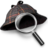 Pixelated image of a dark-colored cat wearing a white-rimmed magnifying glass with a checkered handle, positioned against a light gray background.
