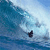 Pixelated static image of a surfer riding a large ocean wave under a light blue sky, with the surfer positioned near the bottom right and the wave dominating the left side.