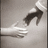 Pixelated grayscale image of a hand reaching toward a dark, curved object against a light background.