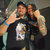 Two pixelated figures in dark clothing pose closely together, one making a hand gesture with a blue wristband visible.