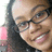 Pixelated close-up of a person with dark hair, glasses, and a black top against a light background.