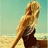 Pixelated image of a person with light brown hair wearing a dark brown one-piece swimsuit on a beach with light blue sky background.