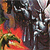 A static pixelated image shows a figure with a red lower body and green foliage-like elements against a dark background with metallic and light-colored shapes.
