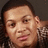 Pixelated close-up of a person with dark hair, light skin tone, and visible facial features including eyes, nose, mouth, and ear against a dark background.