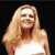 Pixelated image of a person with long blonde hair wearing a white sleeveless top against a dark background.