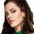 A pixelated close-up of a person with long brown hair wearing a green top, showing partial facial features including eyes, nose, and lips.