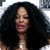 Pixelated close-up of a person with voluminous dark curly hair, light skin, and pink lips, wearing a dark top against a light background.