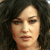 Pixelated close-up of a person's face with dark curly hair, neutral expression, and light skin tone.