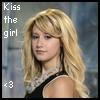 A static image of a woman with long blonde hair wearing a black sleeveless top and a white beaded necklace, with text reading 'Kiss the girl' and a heart symbol on the left side.