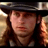 Static 48x48 pixel icon showing a close-up of a person with long brown hair wearing a dark hat and light-colored shirt against a blurred background.