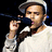 Pixelated image of a person wearing a light-colored cap and white shirt holding a dark microphone against black background.