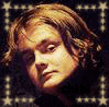 Two side-by-side pixelated images of a person with light brown wavy hair against a dark background with white patterns, one showing slightly different facial expression