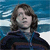 Static pixelated image of a person with shoulder-length brown hair wearing a dark blue jacket against a blurred ocean background.