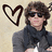 Pixelated image of a person with brown hair wearing dark sunglasses and a black zip-up jacket over a white shirt, next to a large outlined heart symbol on a light beige background.