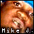 Pixelated static image of a person's face with text "Mike J." at the bottom, rendered in warm tones with blue sky background.