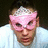 A person wearing a pink mask and white shirt with pixelated text reading "the coolest person you'll evr meet is my BROTHER!" on black background.