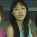 showing a person with long dark hair wearing a light blue sleeveless top, with pink and gray background elements