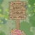 Pixelated sign with multiple lines of text on a wooden post, set against a blurred green background with pink and yellow elements at the bottom.