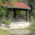 Pixelated static image of a small structure with a red roof, black frame, and light-colored base, set against a green background with blurred foliage.