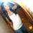 Pixelated image of a figure with brown hair and blue clothing holding an object against a light background.
