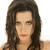 Pixelated image of a person with long dark brown hair, light skin tone, and red lips, cropped to show shoulders and upper chest against a white background.