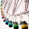 A Ferris wheel with multiple colored passenger cars suspended from its circular frame, viewed from a low angle against a light background.