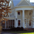 Pixelated image of a white building with columns, brown tree on left, blue sky background, and yellow ground strip at bottom.