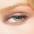 A close-up of a human eye with light skin tone, featuring visible eyelashes and an iris showing subtle color variations.